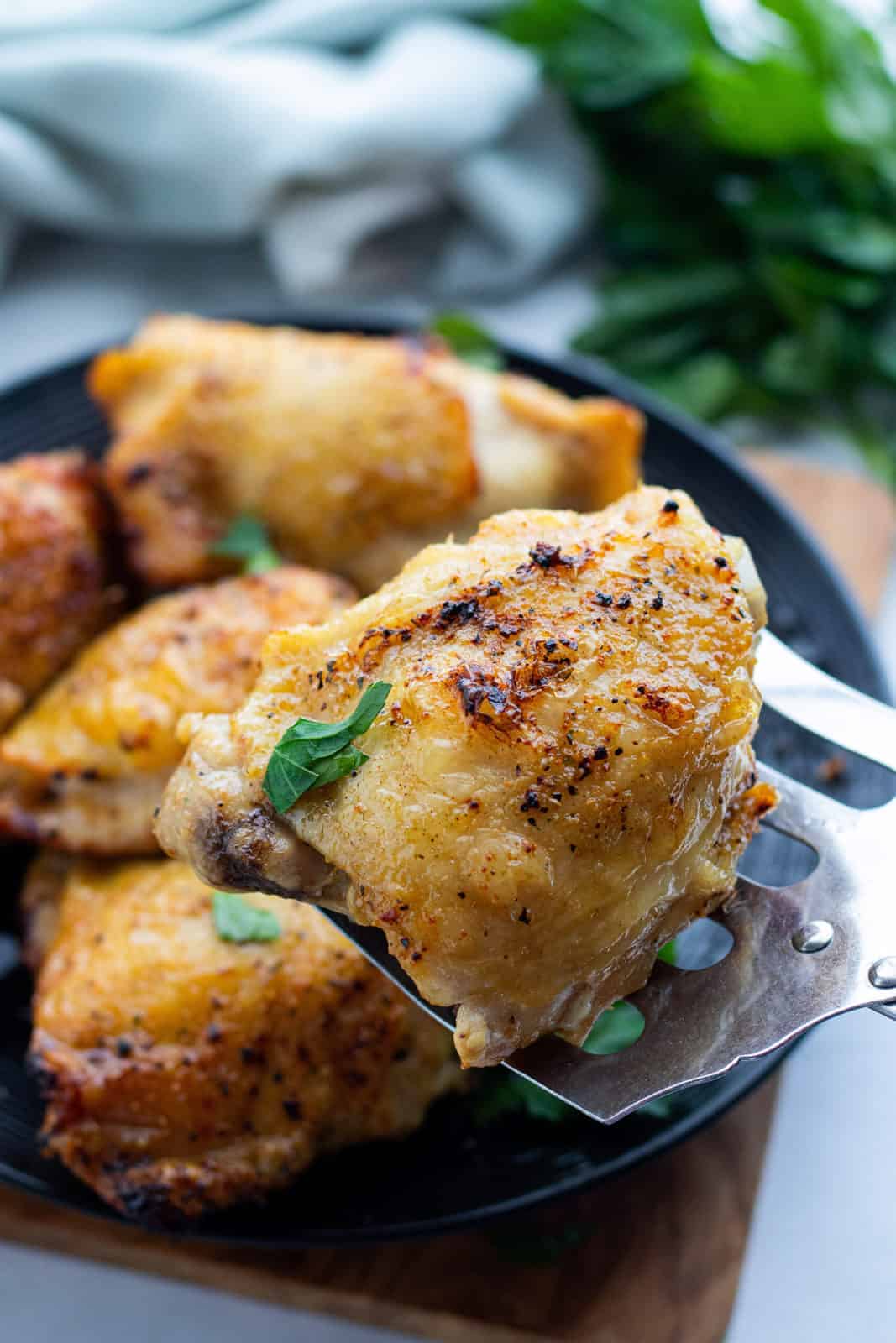 Air Fryer Chicken Thighs showing chicken thighs on a serving platter with a spatula scooping up one chicken thigh on top of a countertop.