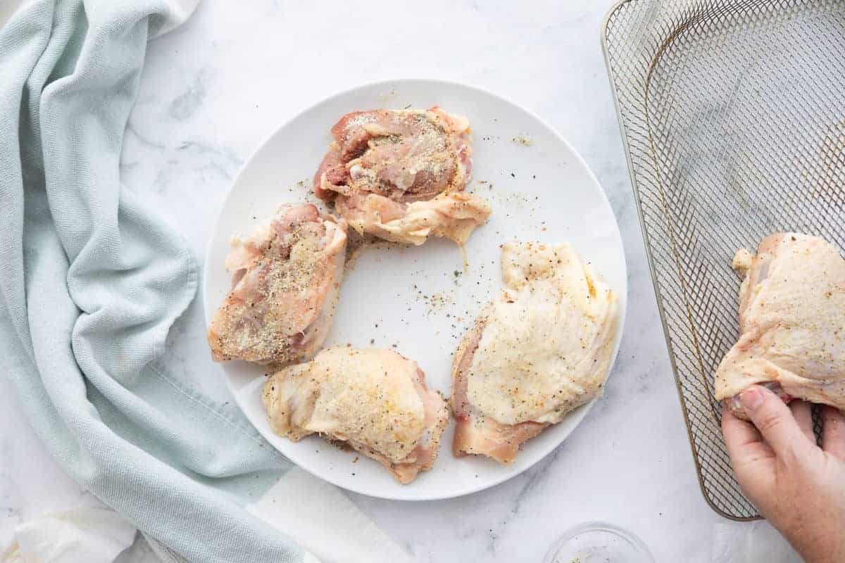 Air Fryer Ranch Chicken Thighs showing raw chicken thighs on a white plate with an air fryer rack next to the plate all on top of a countertop.