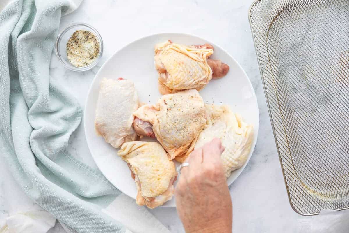raw chicken thighs being seasoned