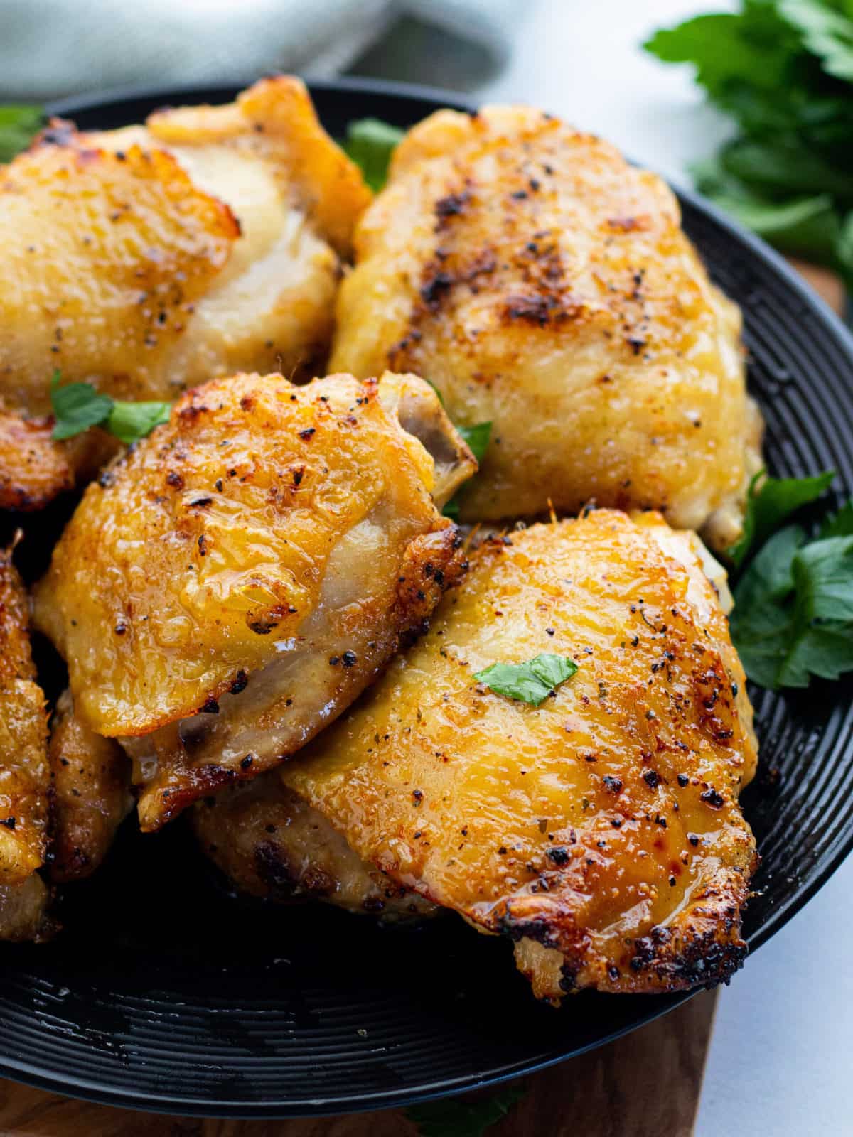 Air Fryer Chicken Thighs showing chicken thighs on a serving platter with a blue towel under the plate all on top of a countertop.