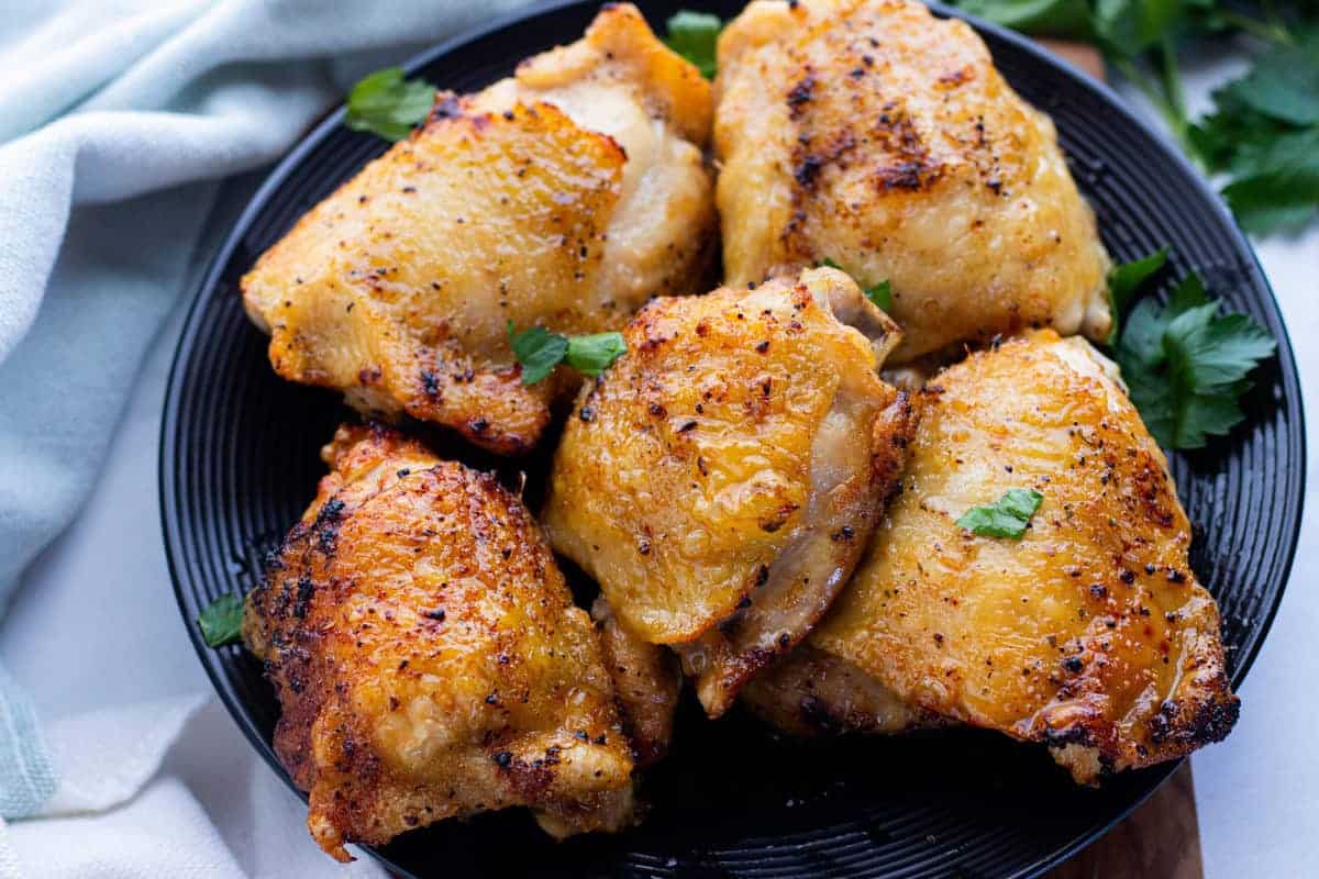 Air Fryer Chicken Thighs showing chicken thighs on a serving platter with a blue towel under the plate all on top of a countertop.