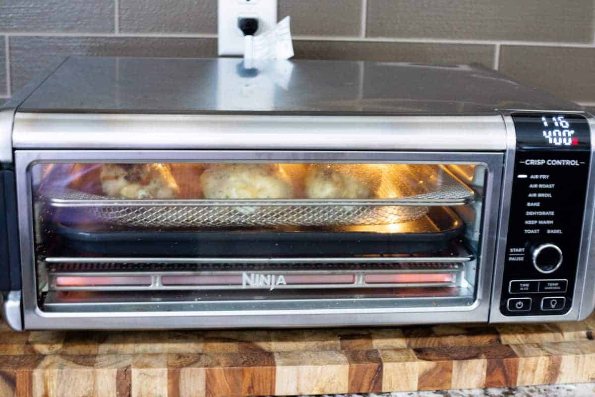 A Ninja Foodi Air Fryer Oven filled with chicken thighs on a countertop.