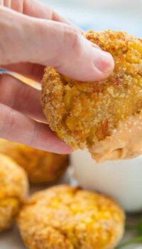 Salmon patties shown on a white plate next to a dip with a hand holding a freshly dipped patty.