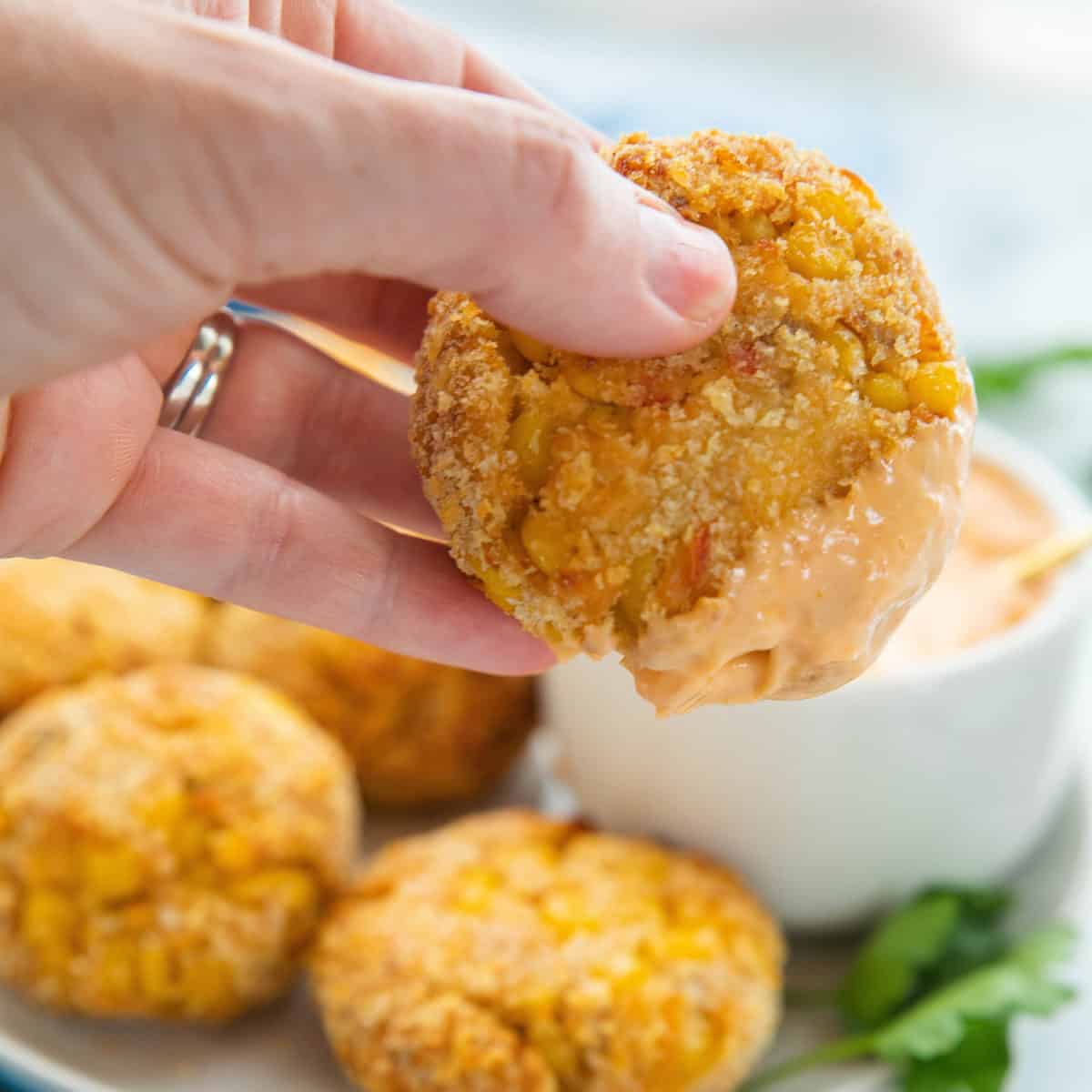 Salmon patties shown on a white plate next to a dip with a hand holding a freshly dipped patty.