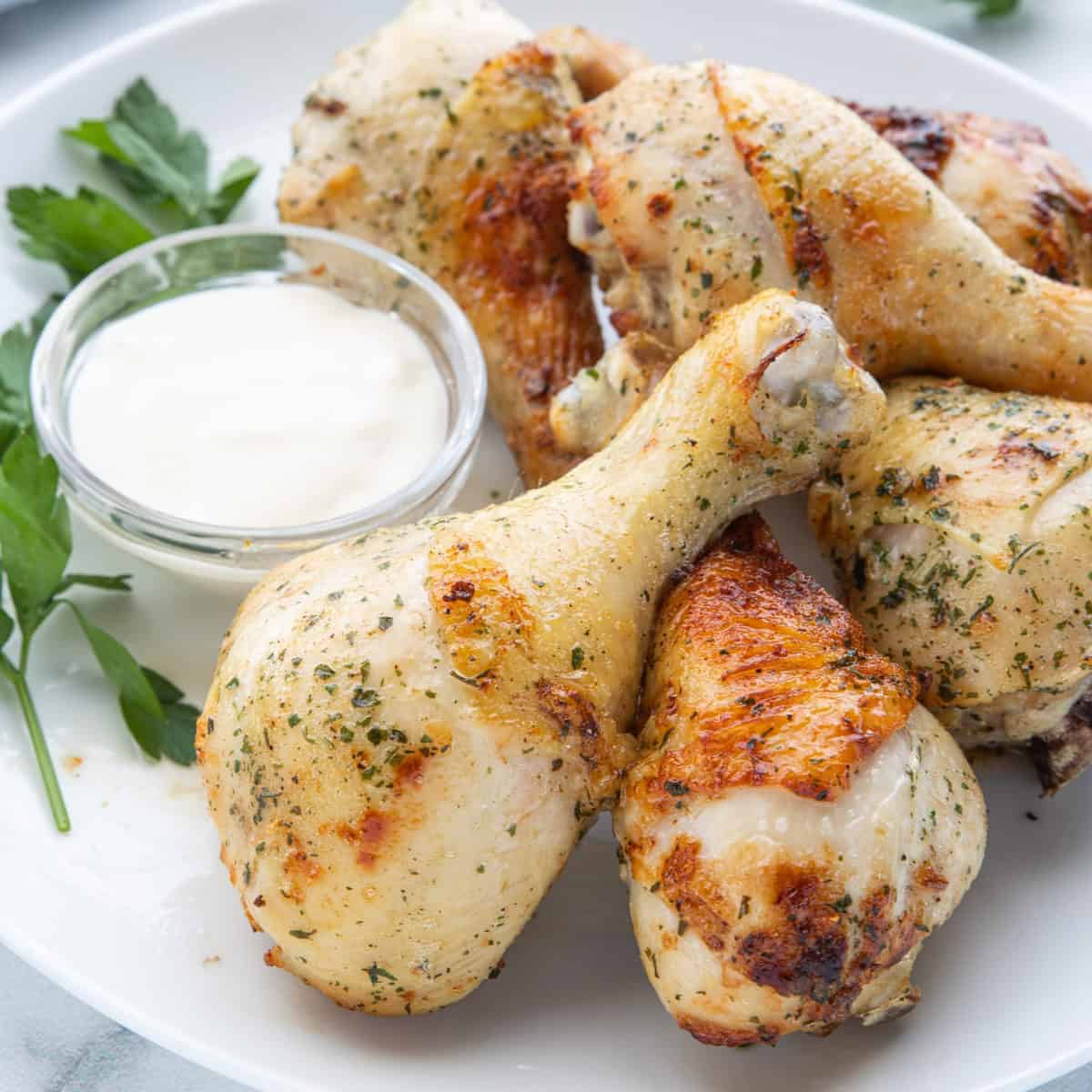 Air fried chicken drumsticks shown stacked on a white plate with herbs on top.
