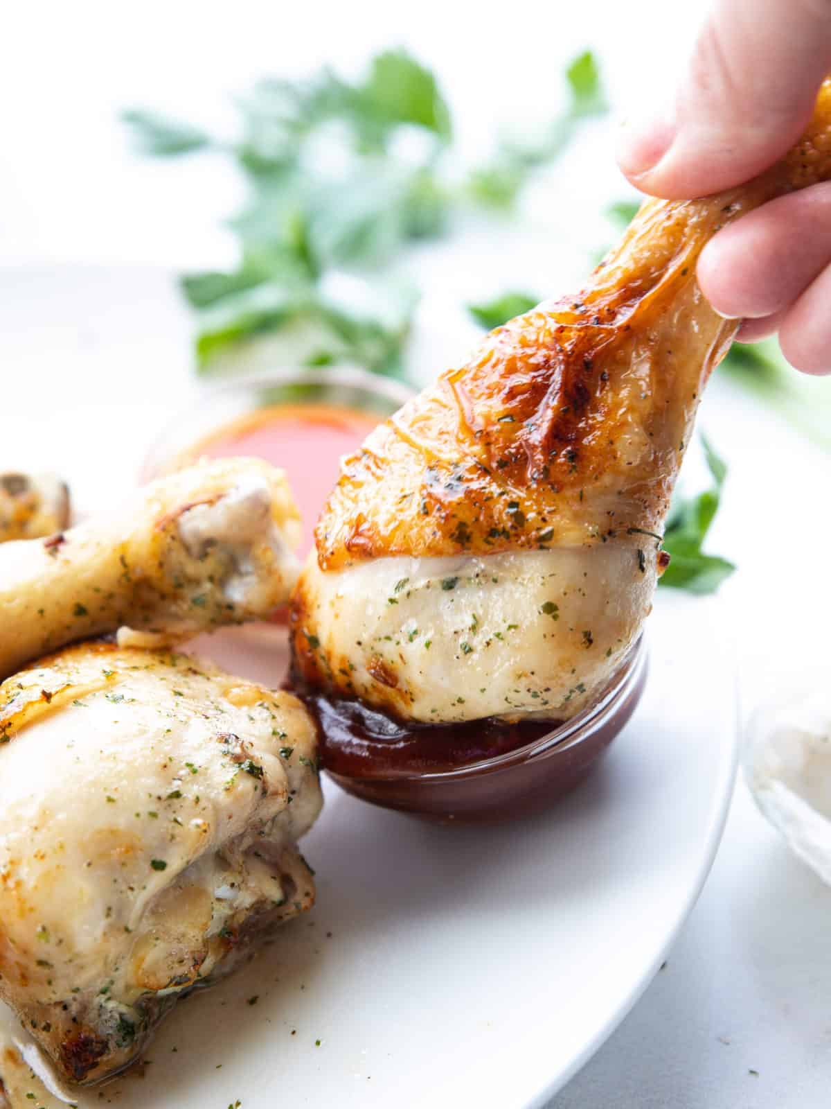Air Fryer Chicken Legs showing a chicken drumstick being dunked into a dipping sauce.