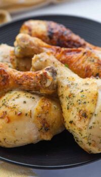 Chicken drumsticks shown cooked and stacked on a black plate.