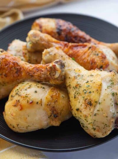 Chicken drumsticks shown cooked and stacked on a black plate.