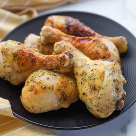 Chicken drumsticks shown cooked and stacked on a black plate.