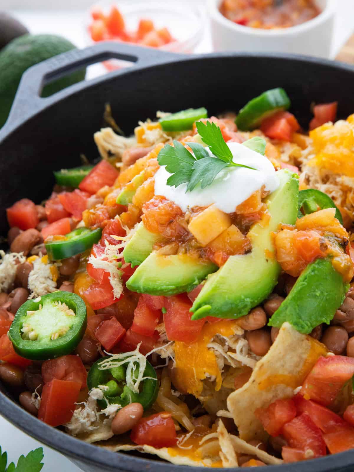 Shredded Chicken Skillet Nachos showing nachos with toppings in a cast iron pan. 