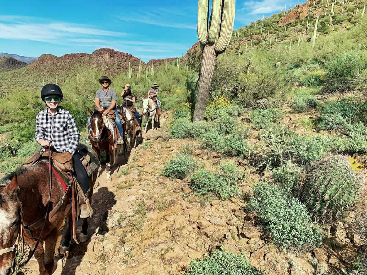 White Stallion Ranch, the Best All-Inclusive Resort in Arizona showing a family of four riding horses through the mountainous region of Arizona. 