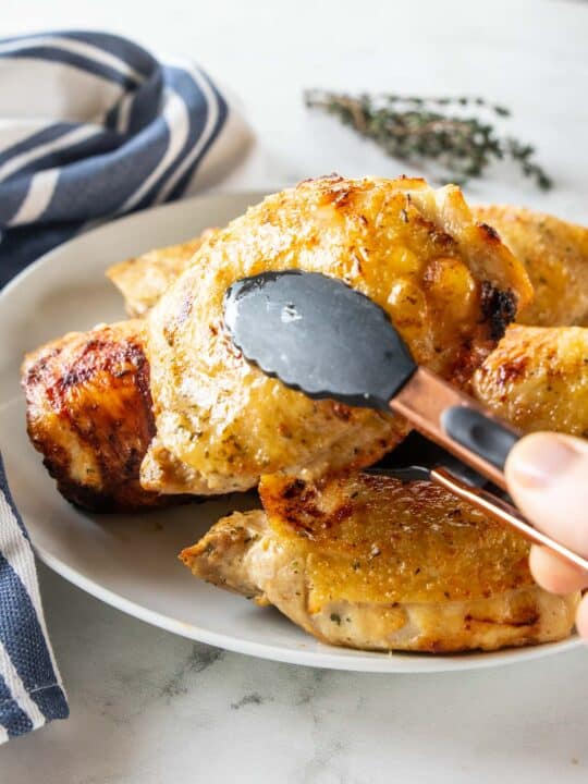 Crispy chicken thigh held with a tong on a white plate. 