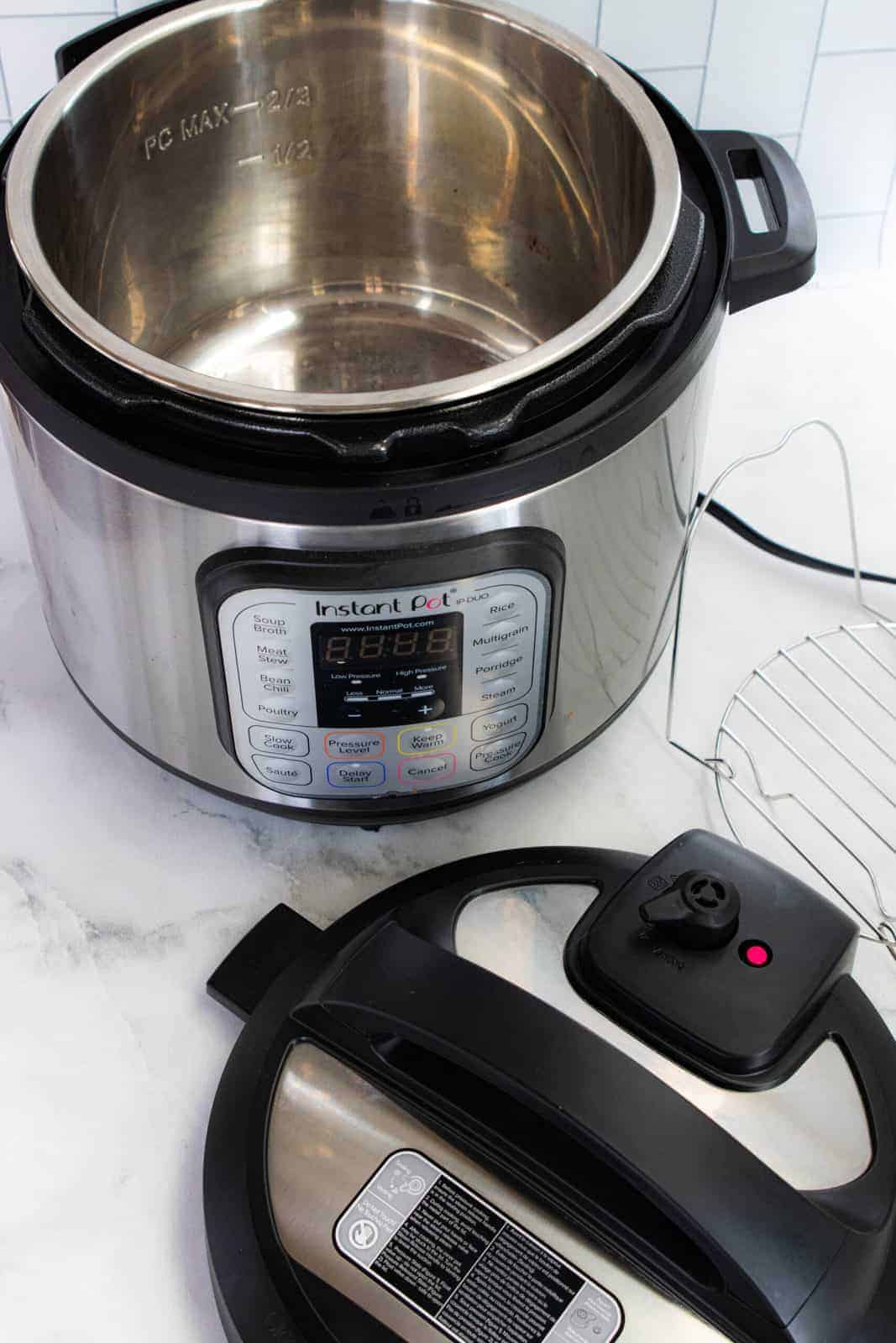 Instant pot showing the unit, wire insert, and lid on a white marble surface.