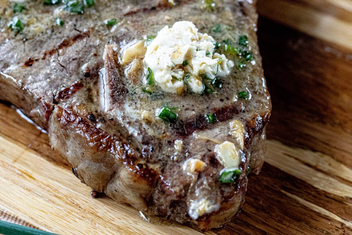 A close up show of a porterhouse steak with compound butter for steak melting on top.