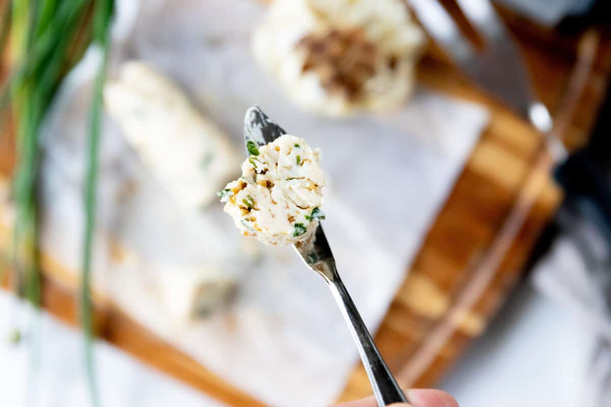 A butter knife holding a slice of compound butter for steak up close to the camera with the rest of the butter blurred in the back.