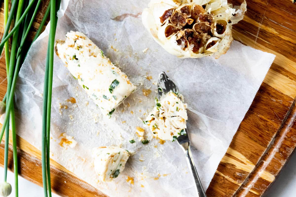 Compound butter shown sliced on wax paper with chives and roasted garlic next to it.