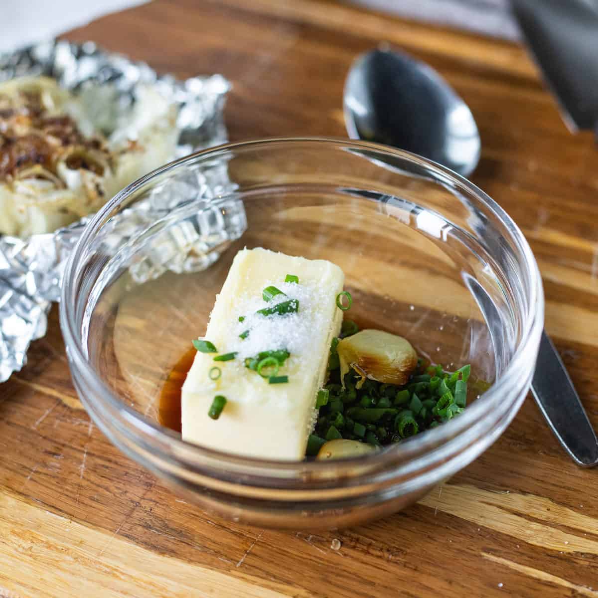 butter, chives, salt, and roasted garlic in a clear glass bowl before being mixed.