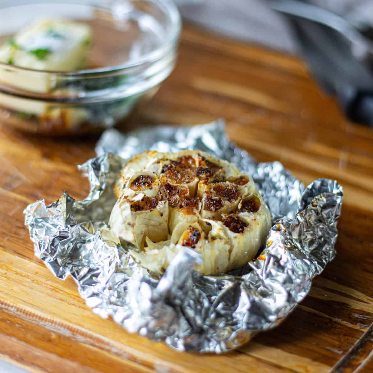 A head of garlic is shown after roasting on the grill in tin foil pulled back.