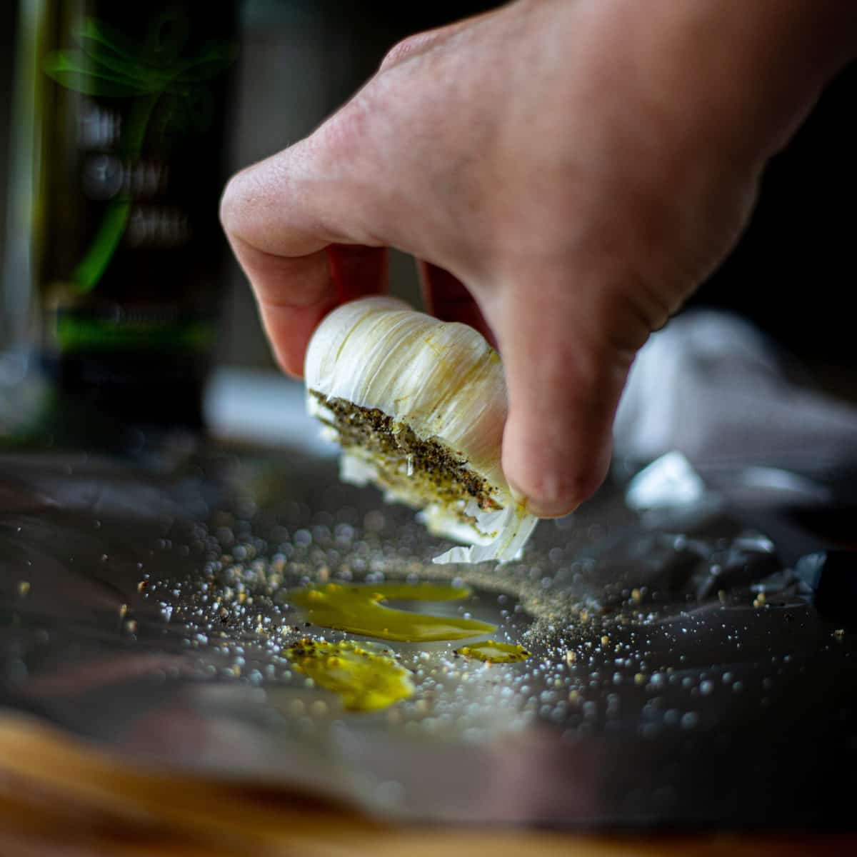 A head of garlic on tin foil with a hand turning it upside down. 