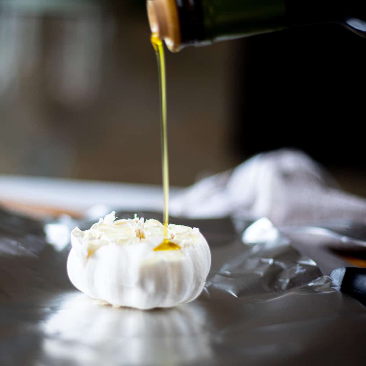 A head of garlic on tin foil with olive oil being drizzled onto it. 