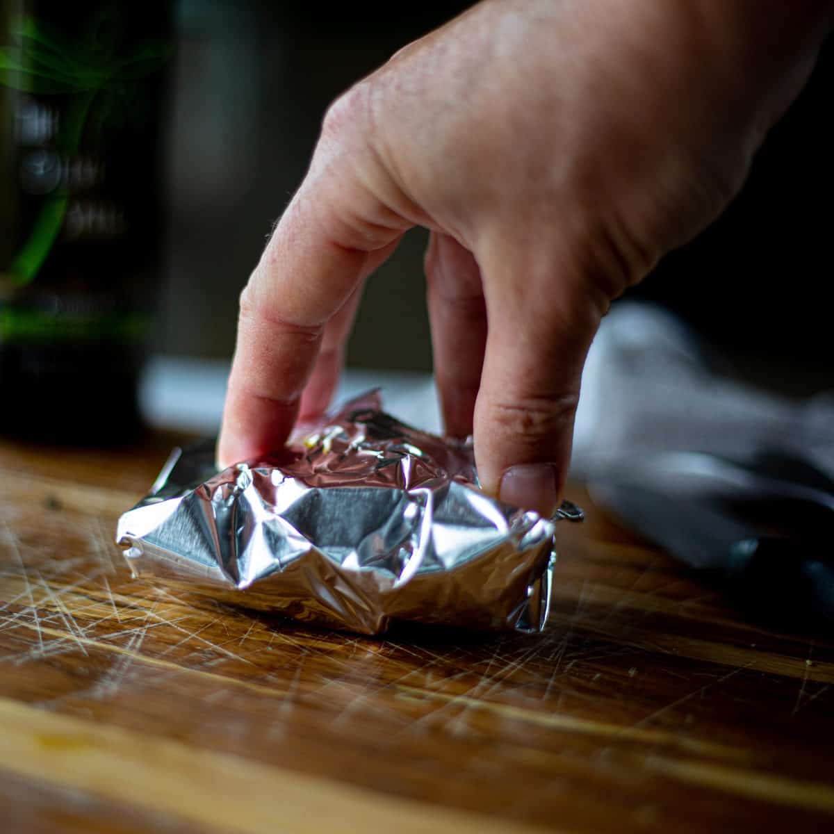 A hand sealing a tin foil packed shut on a cutting board.