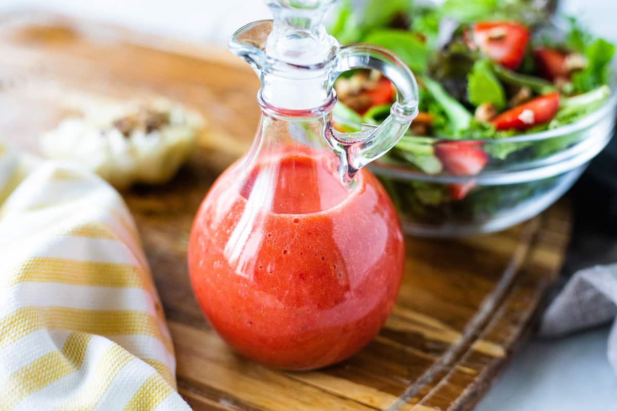 Strawberry Vinaigrette in a clear glass jar next to a lettuce salad. 