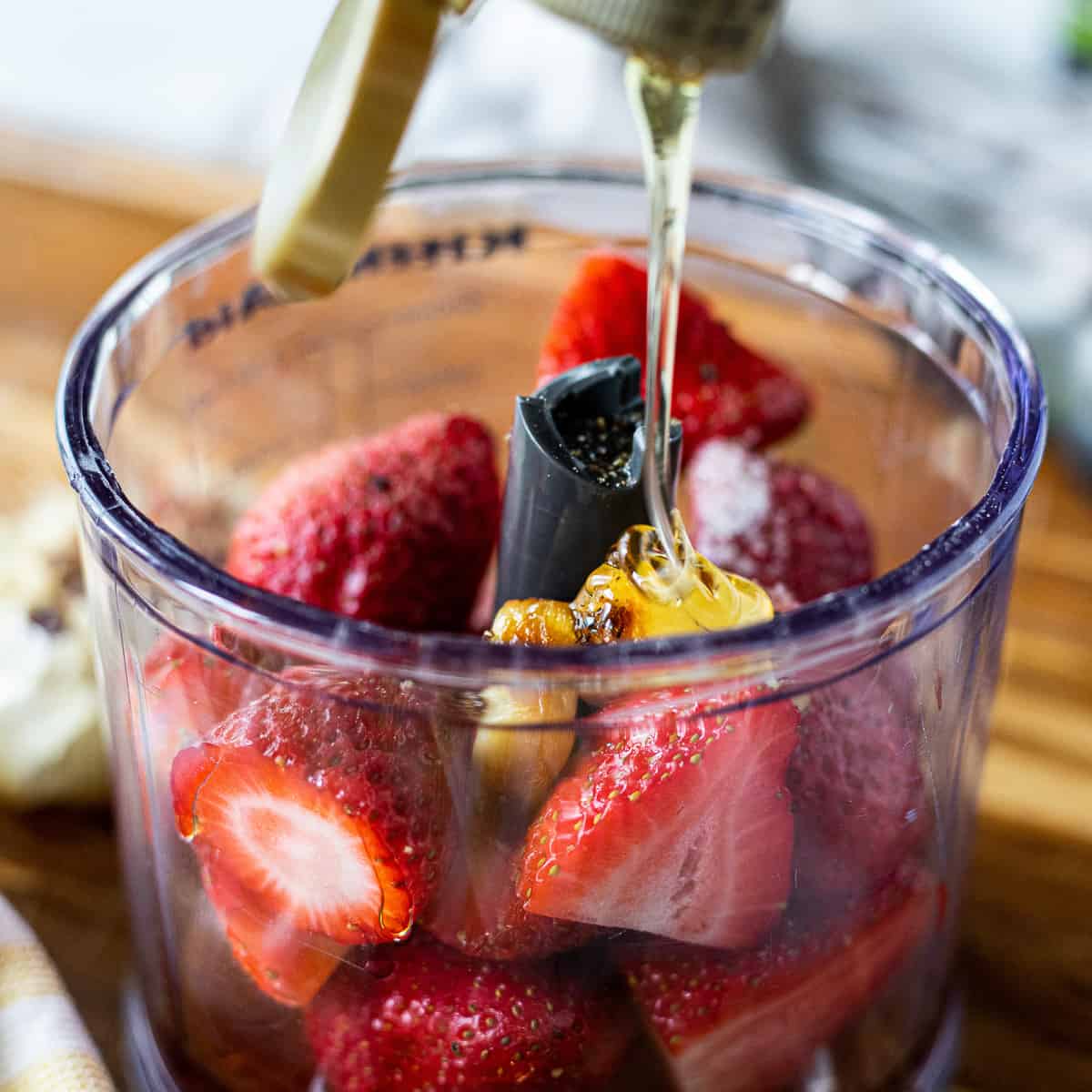 Sliced strawberries, garlic, in a blender with honey being drizzled into it. 