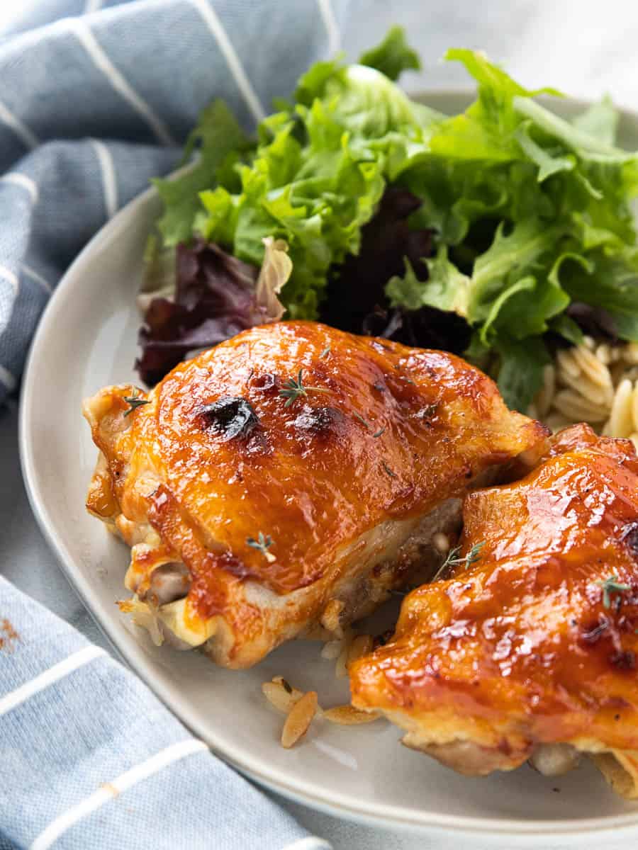 Poached chicken thighs in a serving bowl with cooked rice and lettuce.