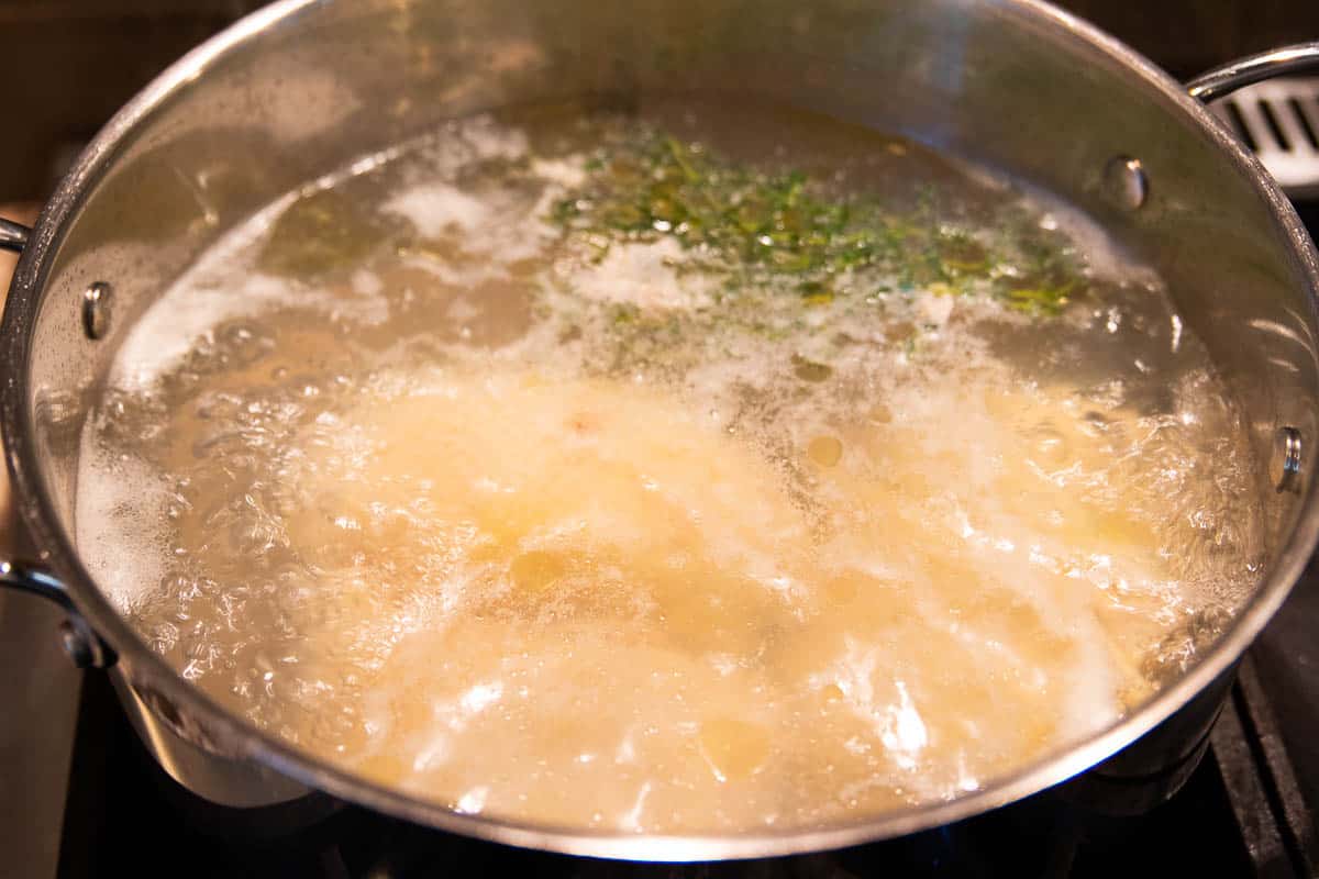 Hähnchenschenkel, die in einem Edelstahltopf mit Wasser, Salz und einem Zweig Thymian kochen.