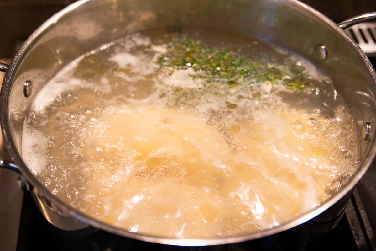 Chicken thighs boiling in a stainless steel stockpot filled with water, salt and a sprig of thyme. 