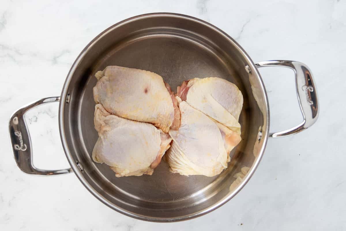 Raw chicken thighs in a stainless steel stockpot.