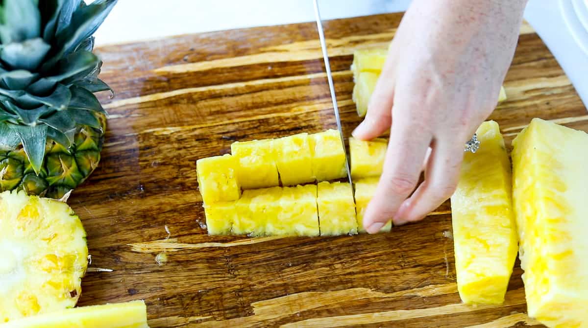 A piece of fresh pineapple is being cut into cubes.