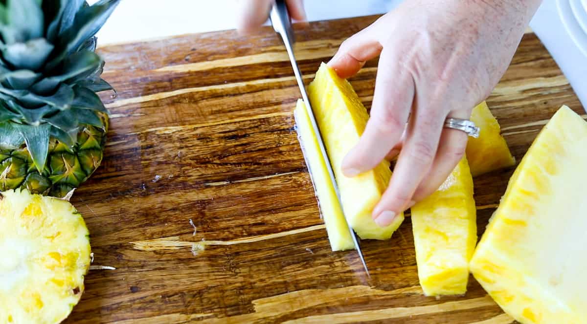 Several pineapple sticks are on a cutting board with the core being cut away from them.