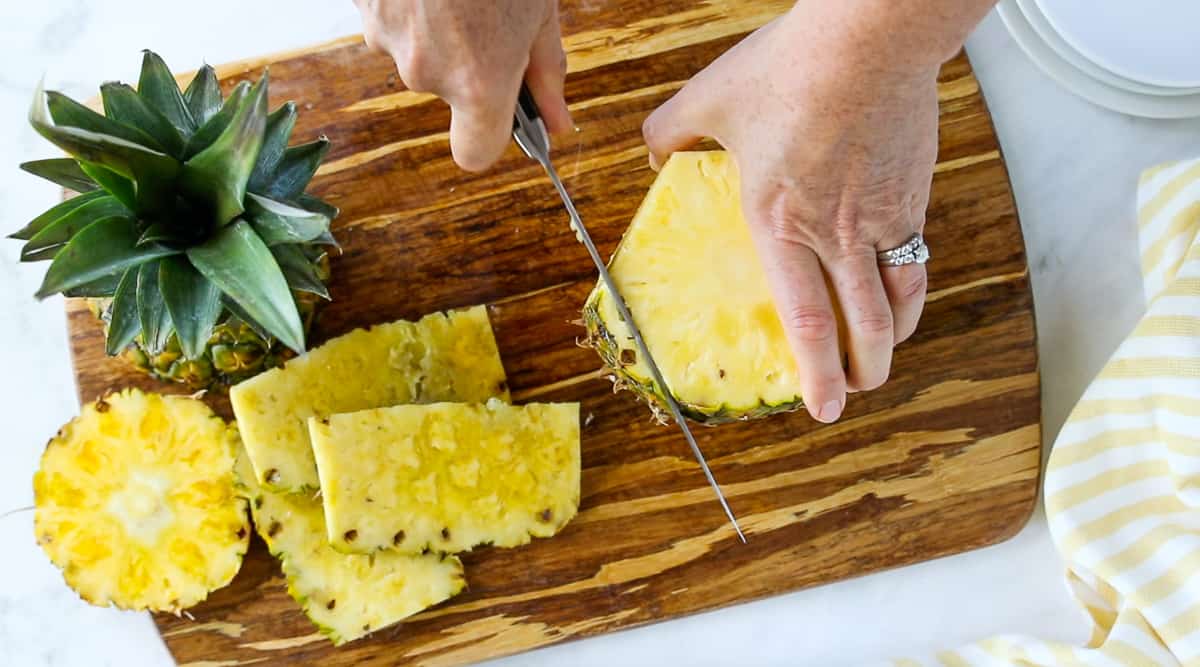 A person holding a piece of pineapple on a cutting board