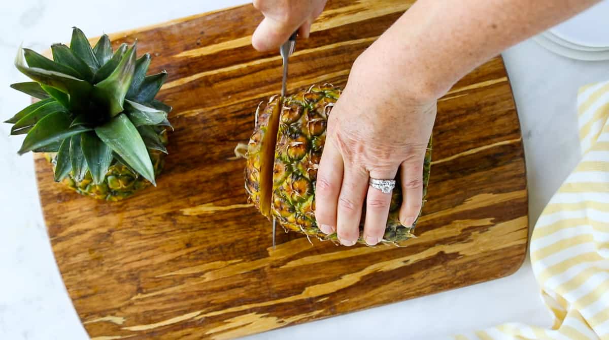 A top down view of a pineapple bottom being cut off with a chefs knife.