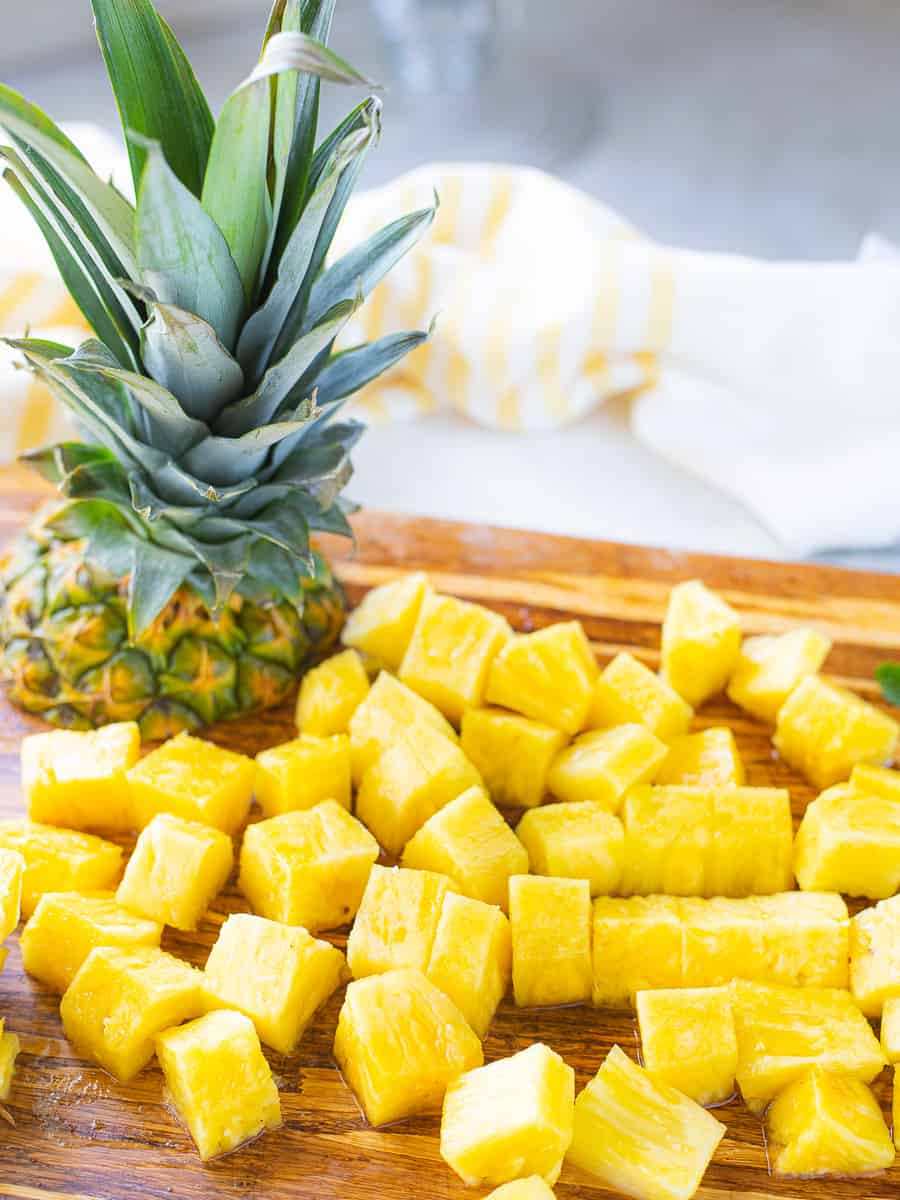 Cubed fresh pineapple on a cutting board next to a top of a pineapple.