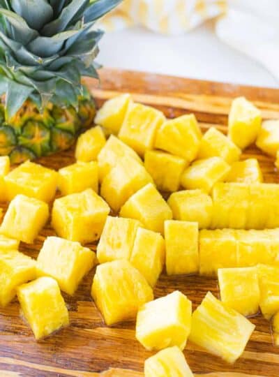pineapple cubes and the top of a pineapple on a cutting board.