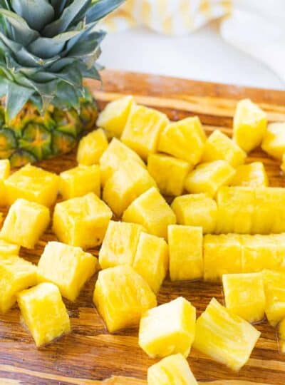 pineapple cubes and the top of a pineapple on a cutting board.
