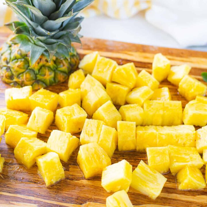 Fresh pineapple cubes on a cutting board next to the top of a pineapple.