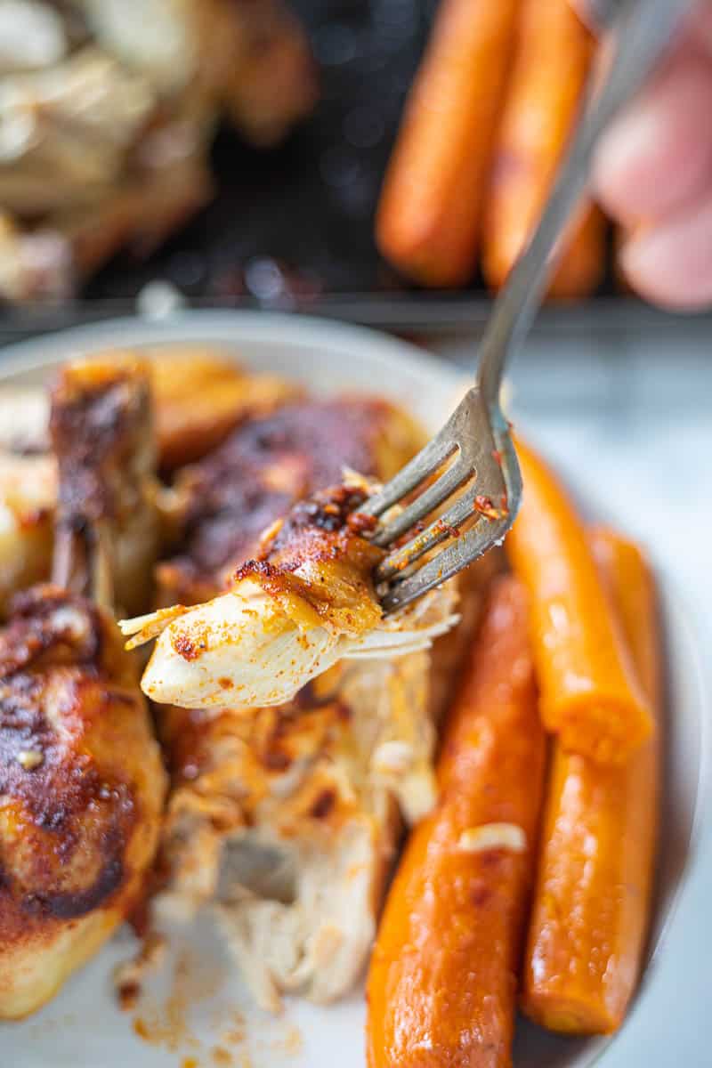 A hand holding a fork that is picking up a piece of cooked chicken.