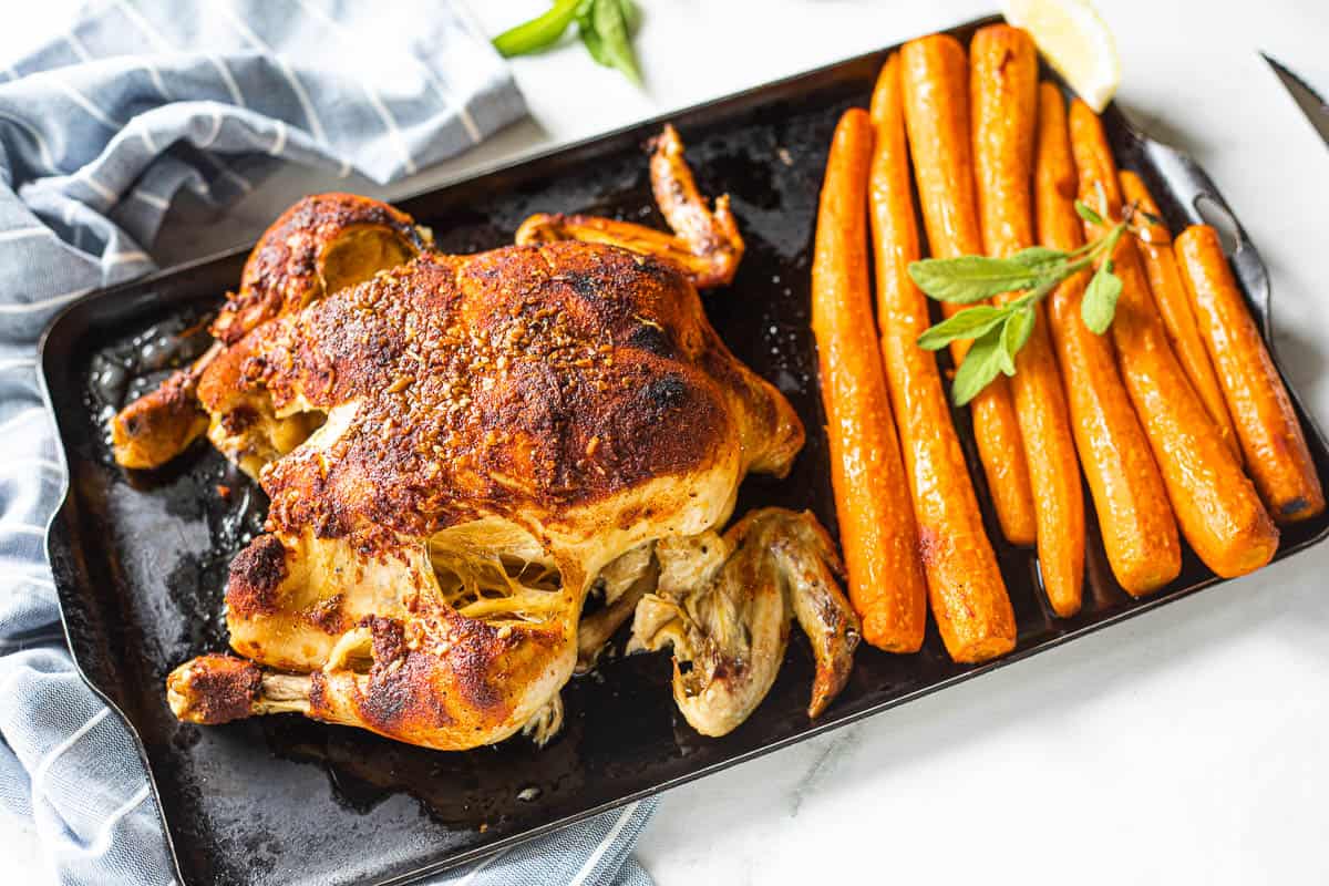 A cooked whole chicken on a baking sheet with cooked carrots.
