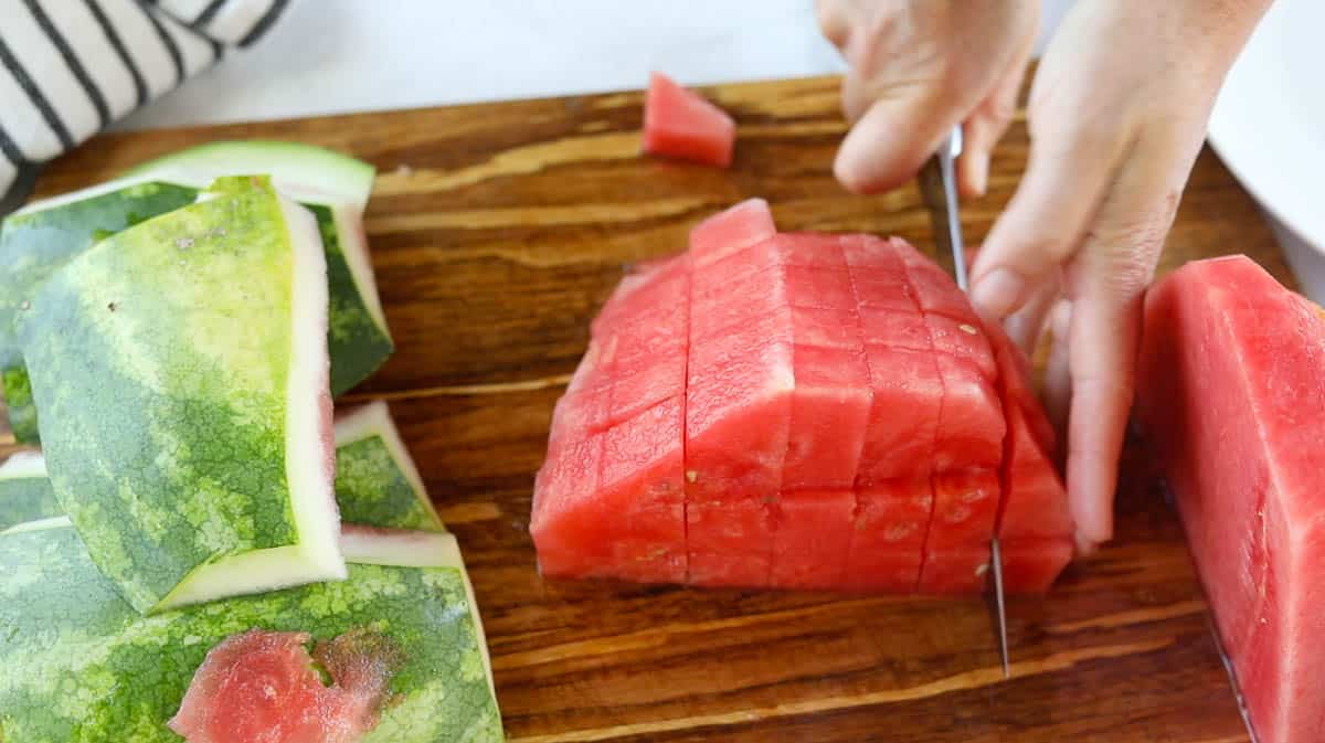 Half a watermelon being cut into cubes with a knife.