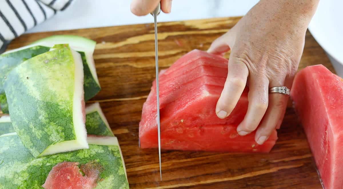 A watermelon half with no rind getting but against the slices already cut.