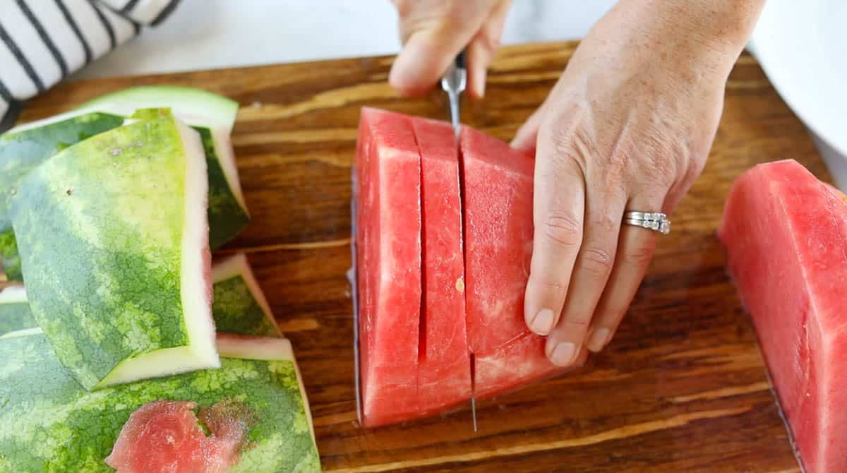 Watermelon half with no rind getting sliced into 1 inch sections again.