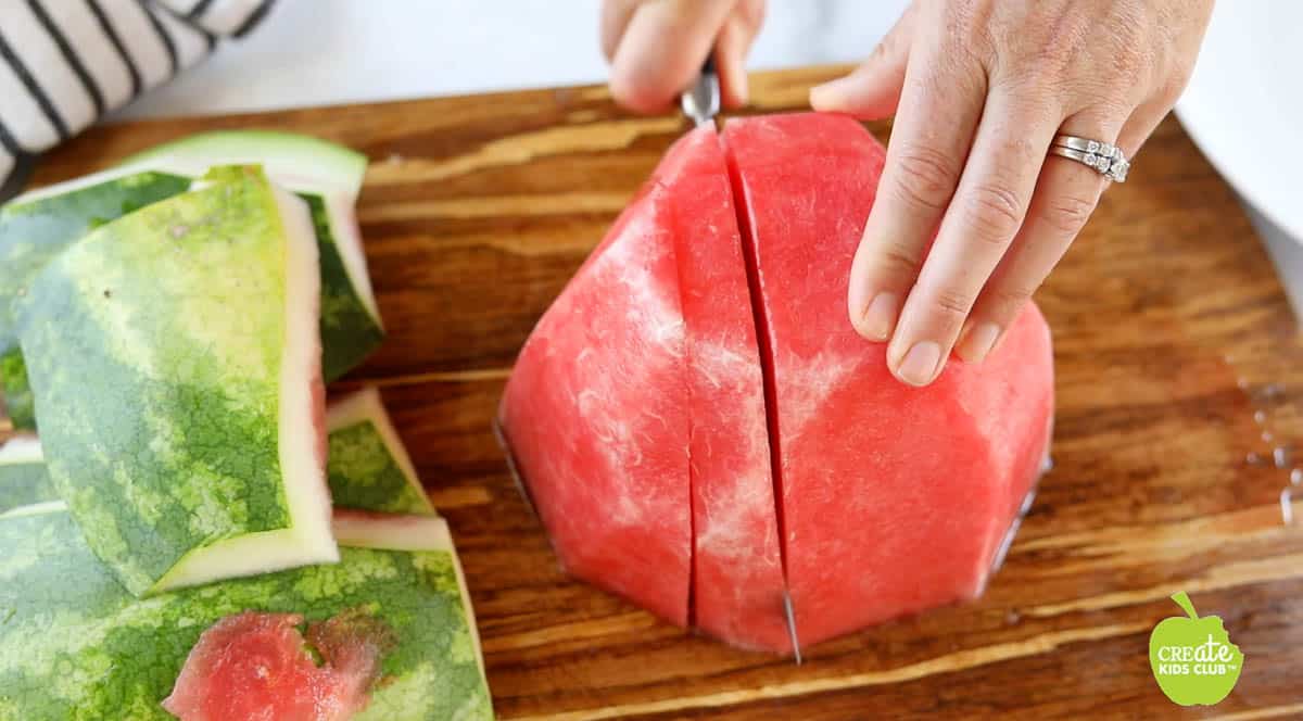 Half of a watermelon with no rind on a cutting board getting cut into large slices.