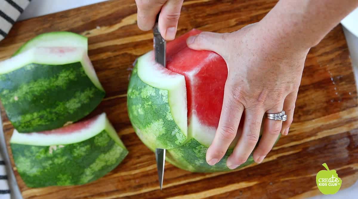 Half a watermelon on a cutting board with the rind getting sliced off.