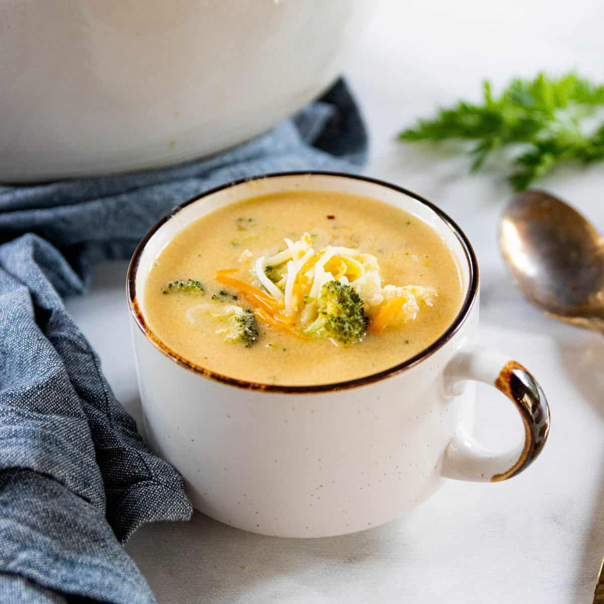 Broccoli cauliflower soup topped with shredded cheese served in a white mug. 
