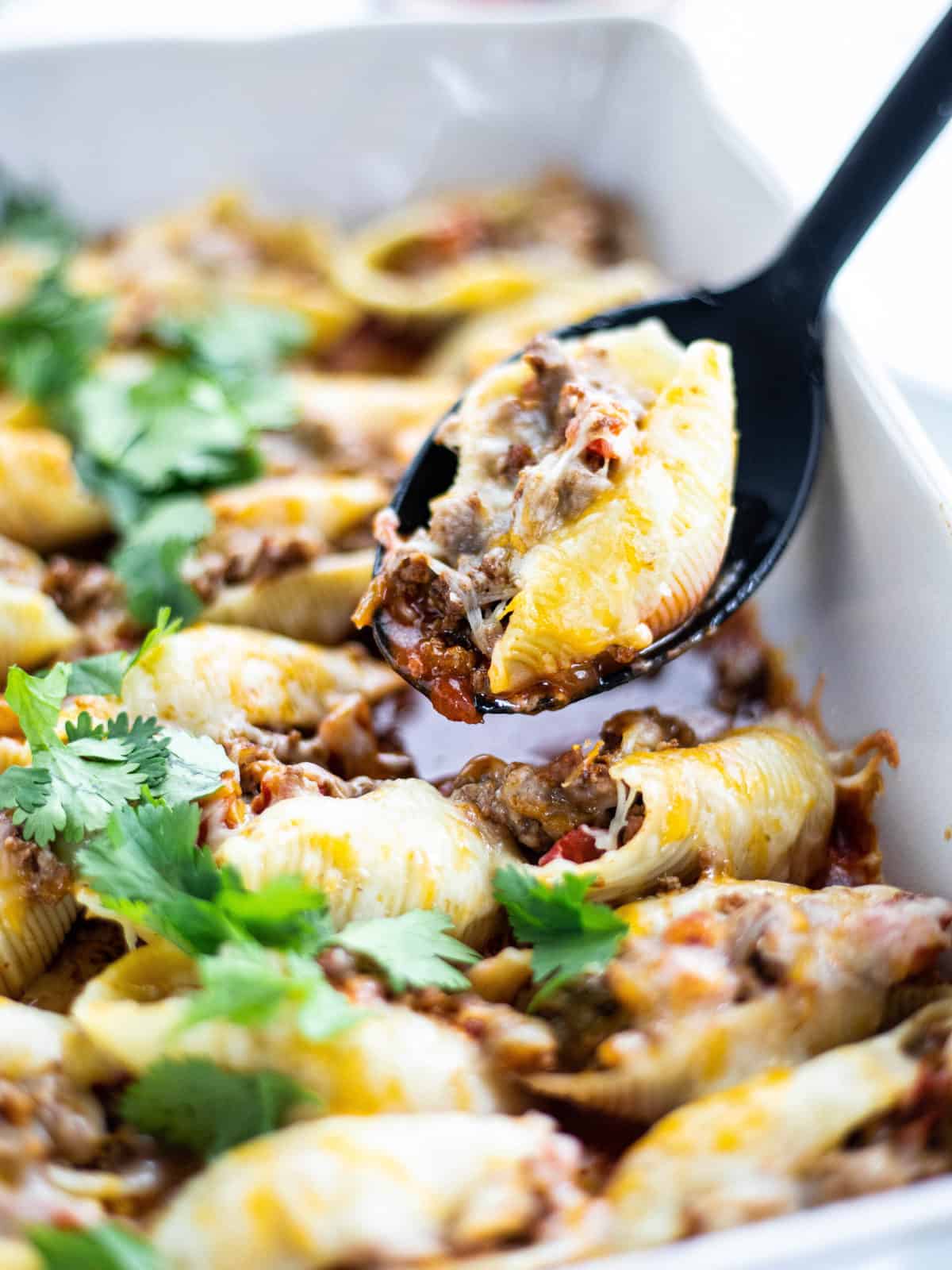 Mexican Stuffed Shells baked in a white casserole dish with a spoon ladling out a shell.