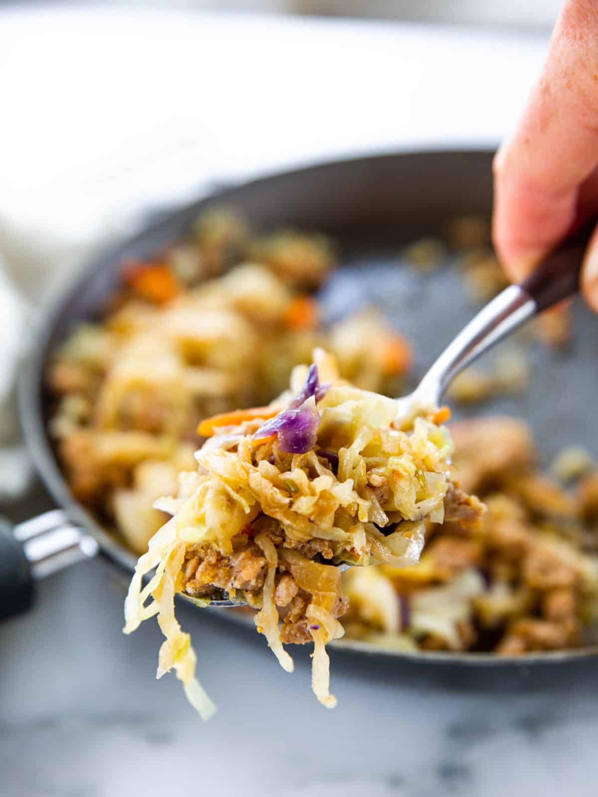 Pork egg roll stuffing shown up close on a serving spoon with the rest of the pan blurred in the background.