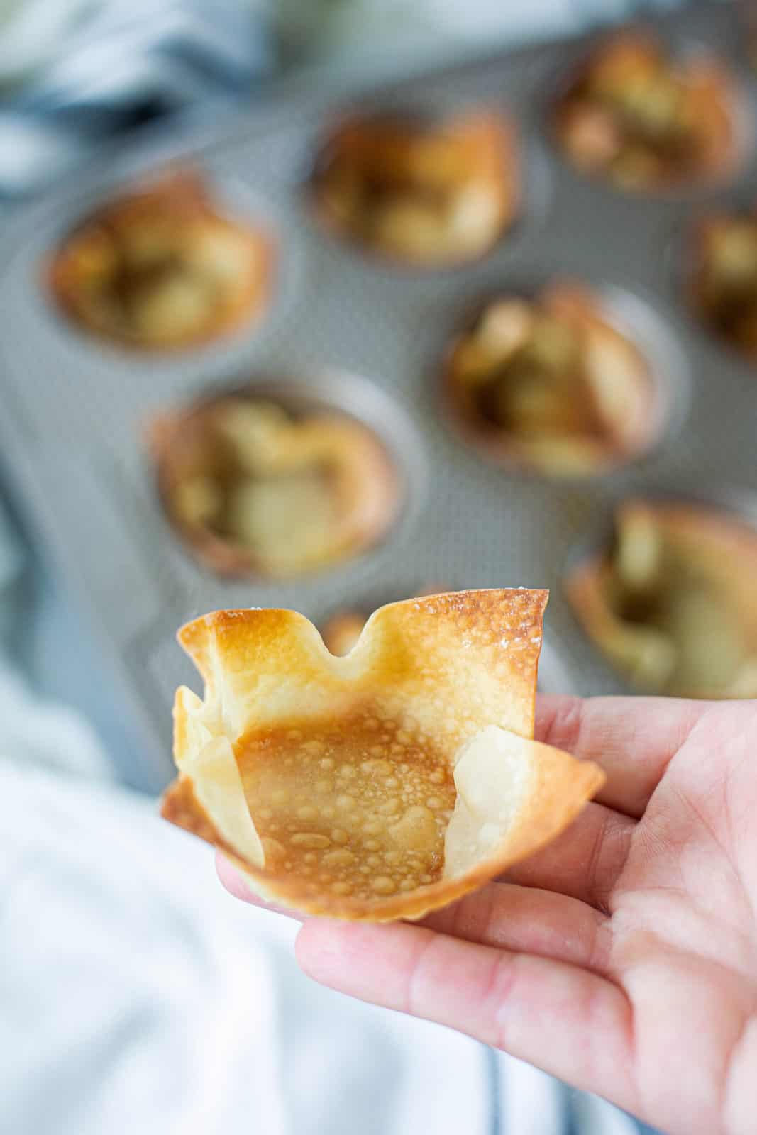 A wonton cup held up close to the camera in a hand after baked showing how crispy it becomes.